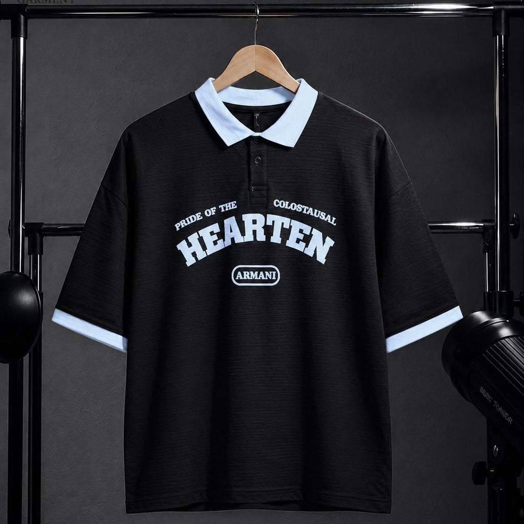 A black short-sleeve polo shirt with a light blue collar and sleeve cuffs, featuring white graphic text on the chest, hanging on a wooden hanger against a dark studio backdrop.