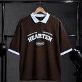 A dark brown short-sleeve polo shirt with a light blue collar and sleeve cuffs, featuring 'HEARTEN' and 'ARMANI' printed in white on the chest, hanging on a wooden hanger against a dark studio backdrop.