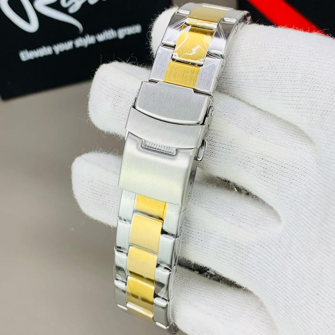 Silver and gold watch on a white glove with 'Risto' branding in the background.